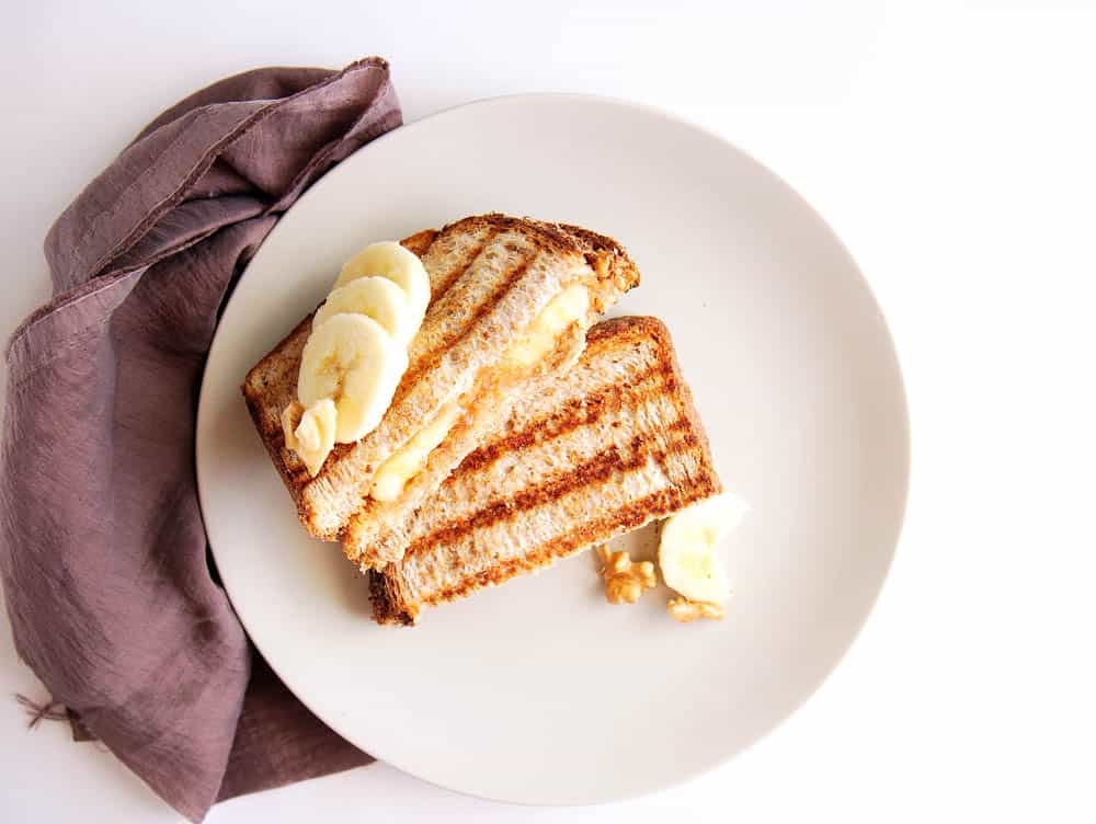 A banana peanut butter sandwich served on a white pate with sliced banana