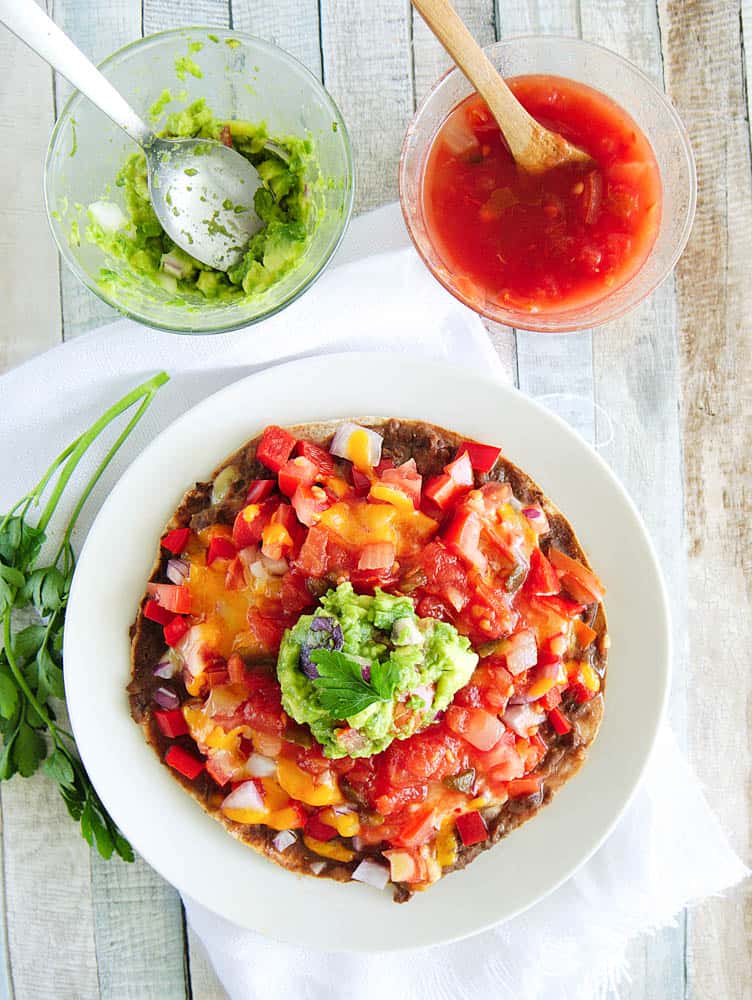 Healthy Copycat Taco Bell Mexican Pizza topped with salsa and guacamole, served on a white plate. guacamole and salsa pictured on the side.