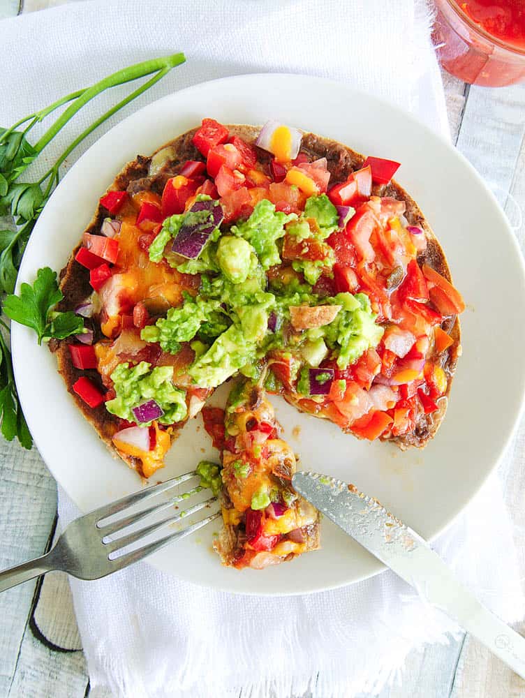 Healthy Copycat Taco Bell Mexican Pizza topped with salsa and guacamole, served on a white plate with a slice cut using a knife and fork
