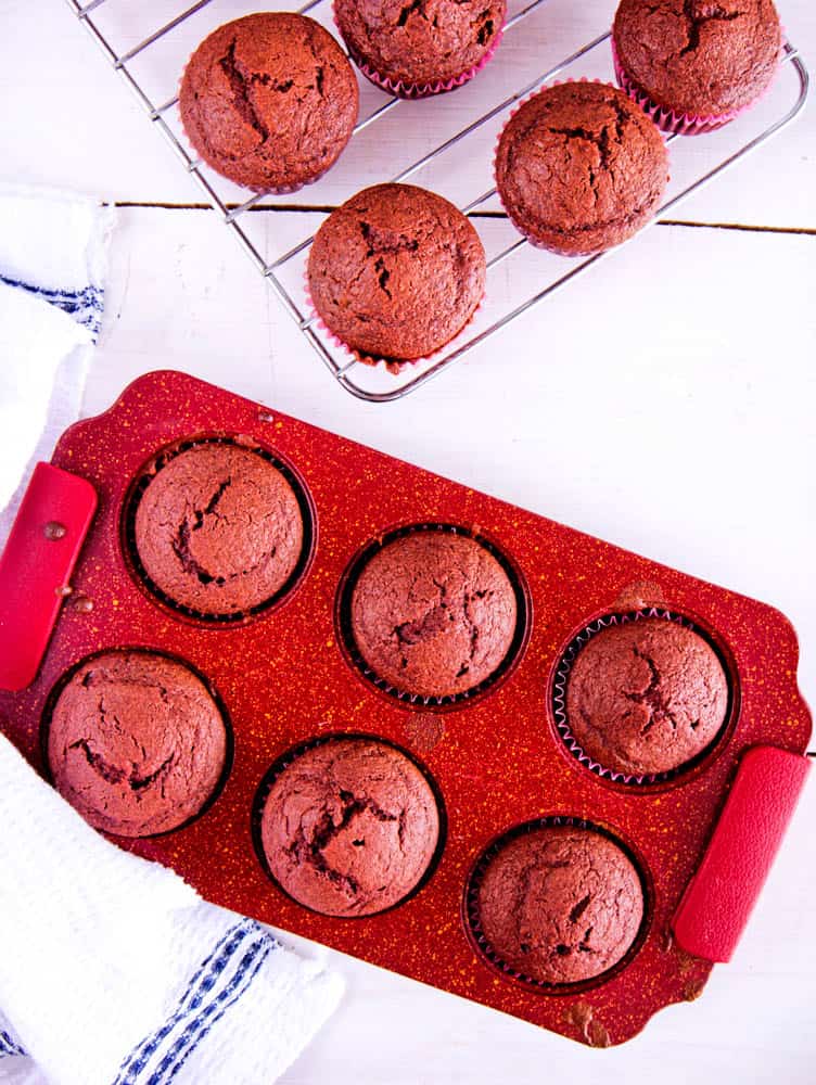 red velvet cupcakes fresh out of the oven on a wire rack against a white background