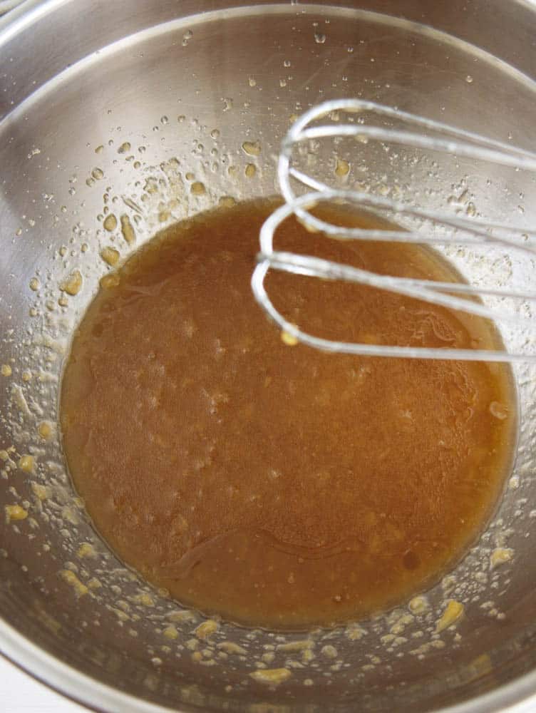 sugar, applesauce and oil whisked in a silver mixing bowl