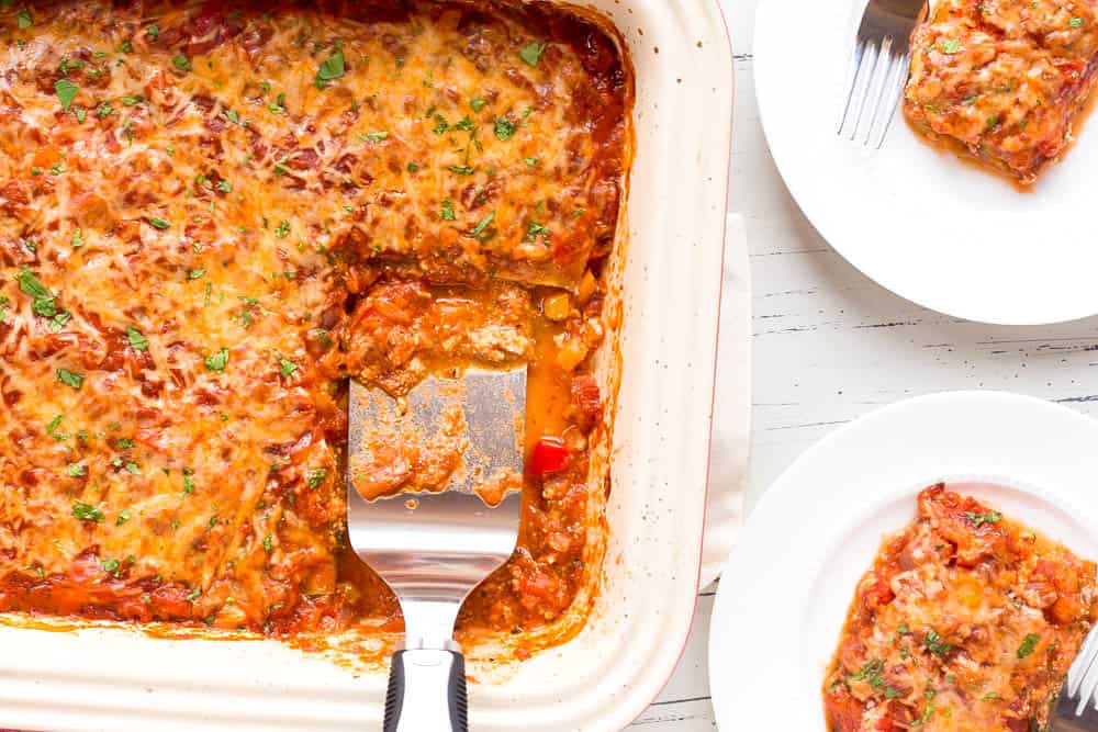 zucchini lasagna served on two white plates with a spatula in he casserole dish