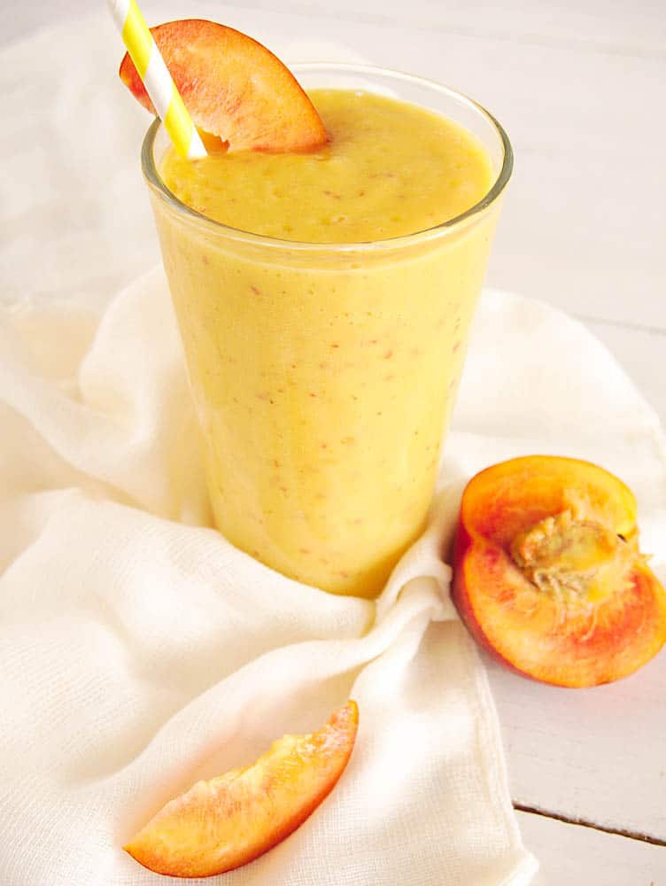A banana peach smoothie garnished with a peach slice