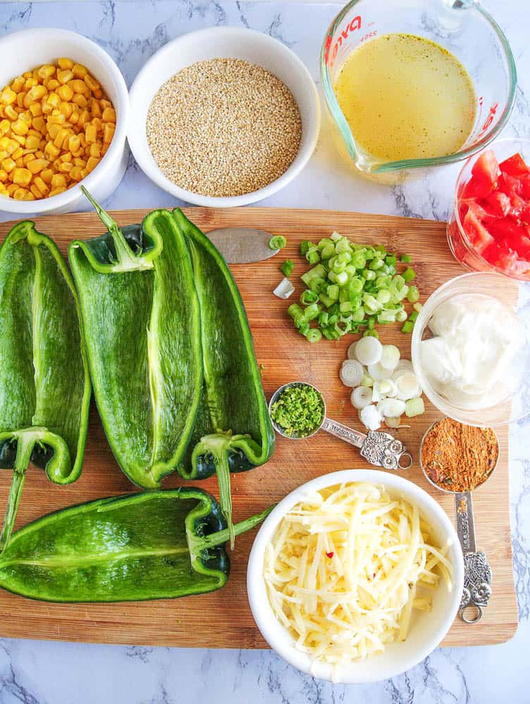 Ingredients for vegetarian stuffed poblano peppers: corn, quinoa, peppers, green onions, cheese, spices, etc. on a wooden cutting board