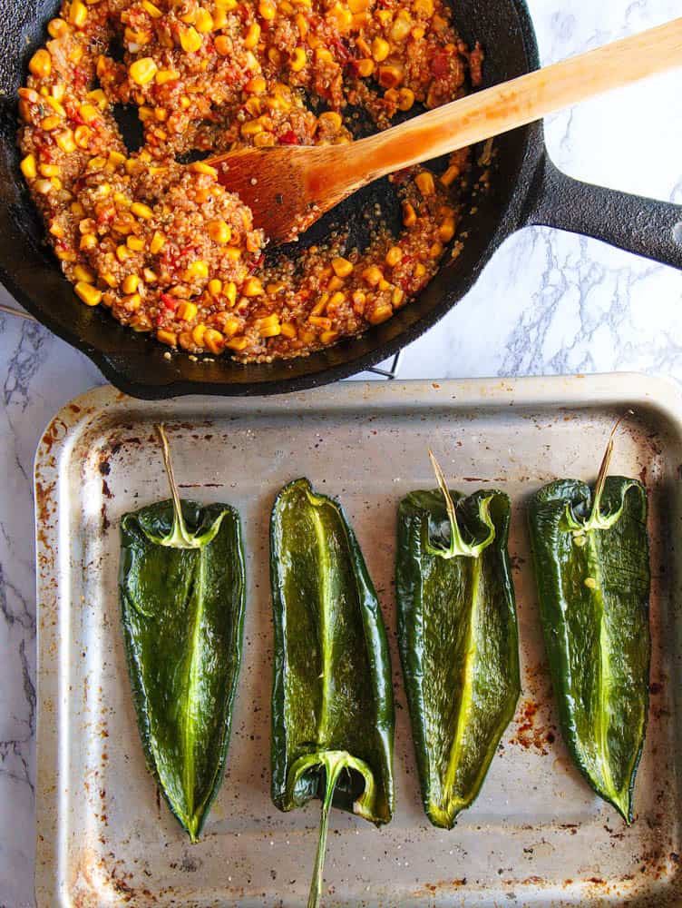 oven baked poblano peppers, unstuffed, on a metal sheet pan. top view of stuffing (corn, tomatoes, quinoa, etc.) on the side.