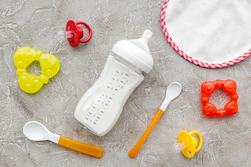 prepared infant formula in a bottle, spoon and toys on agray stone background - top view 