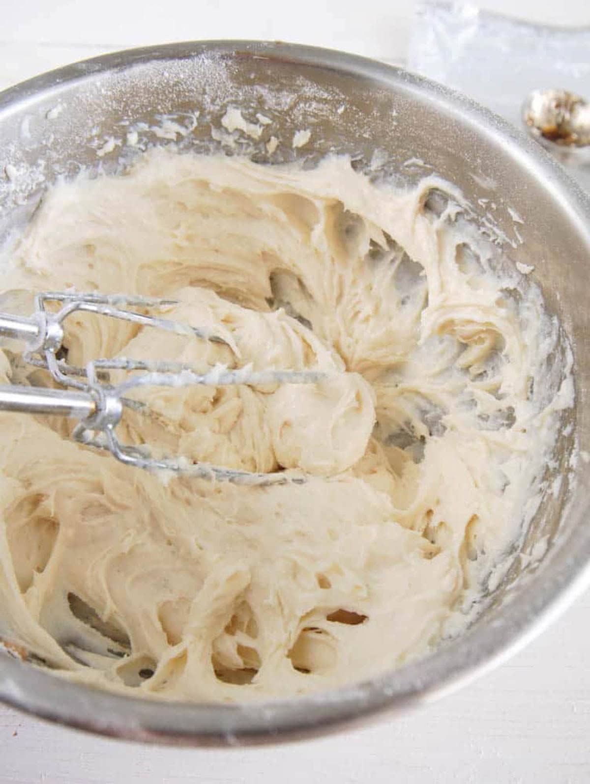 Cupcake icing being mixed with a hand beater in a mixing bowl.