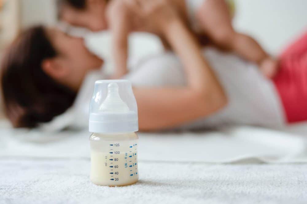 baby bottle filled with milk, with mom and baby in the background