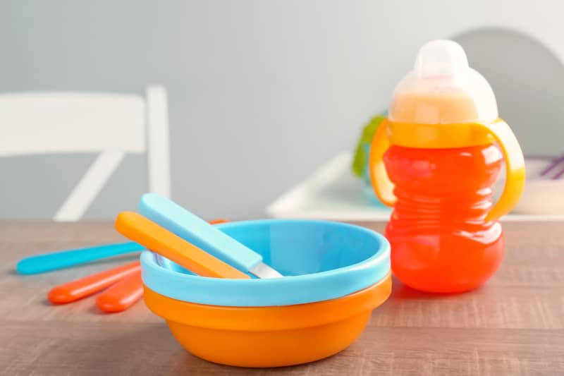 guide to introduce solids: brightly colored baby dishware on wood table - bowls, spoons and sippy cup