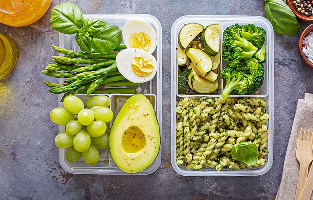 Vegetarian meal prep containers with eggs and pasta with green pesto sauce and vegetables
