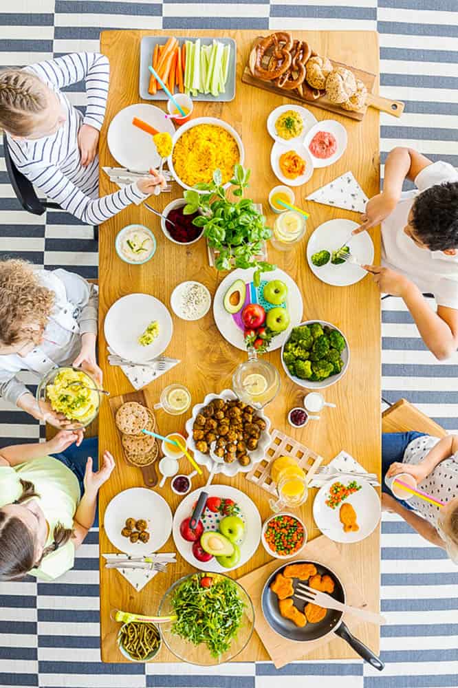 raising a kid who loves vegetables: Top view on table with food. Group of kids eating healthy dinner with vegetables