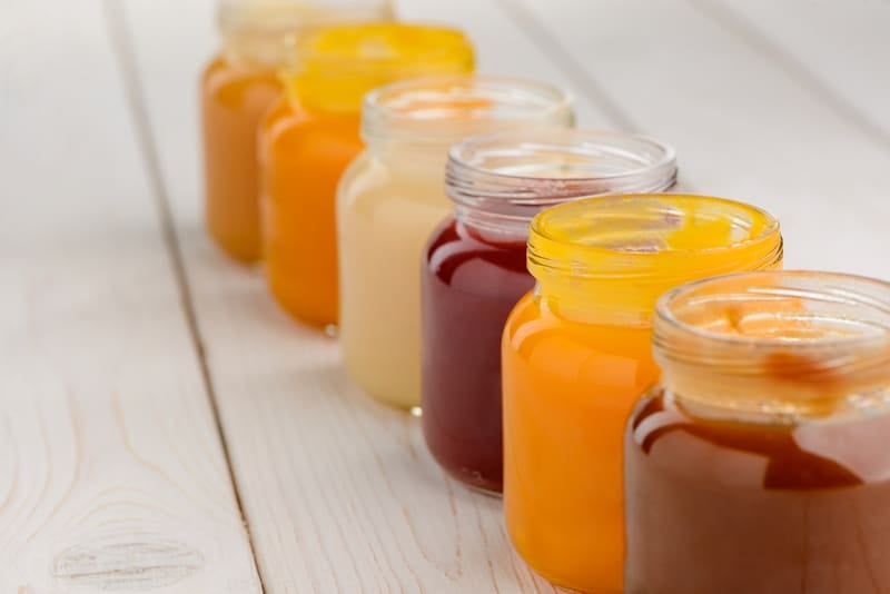guide to introduce solids: Close up on jars of baby food on wooden table, selective focus. Delicious puree made of fruit and vegetables.