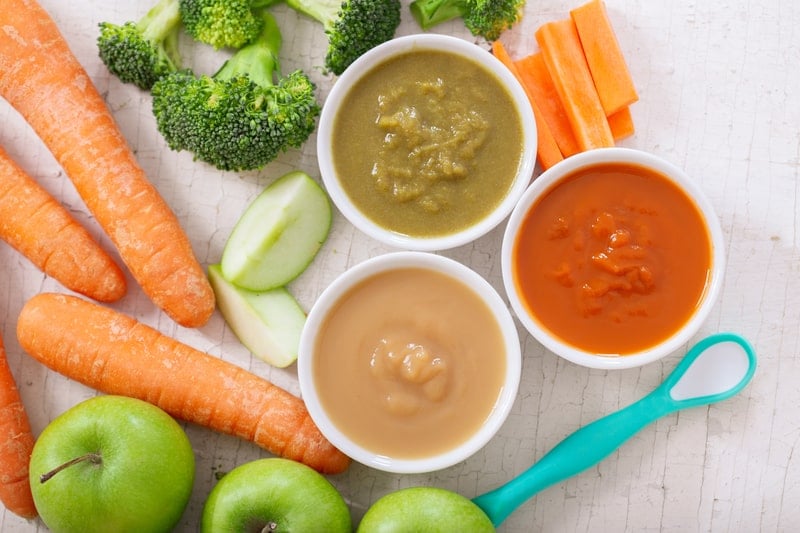 guide to introduce solids: photo of various bowls of fruit and vegetable puree with ingredients for cooking, top view.