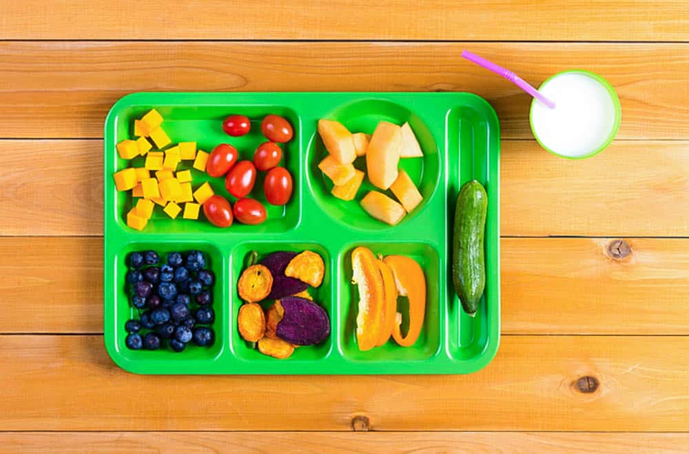 raising a kid who loves vegetables: green lunch tray with a variety of fruits and veggies, against a wood background