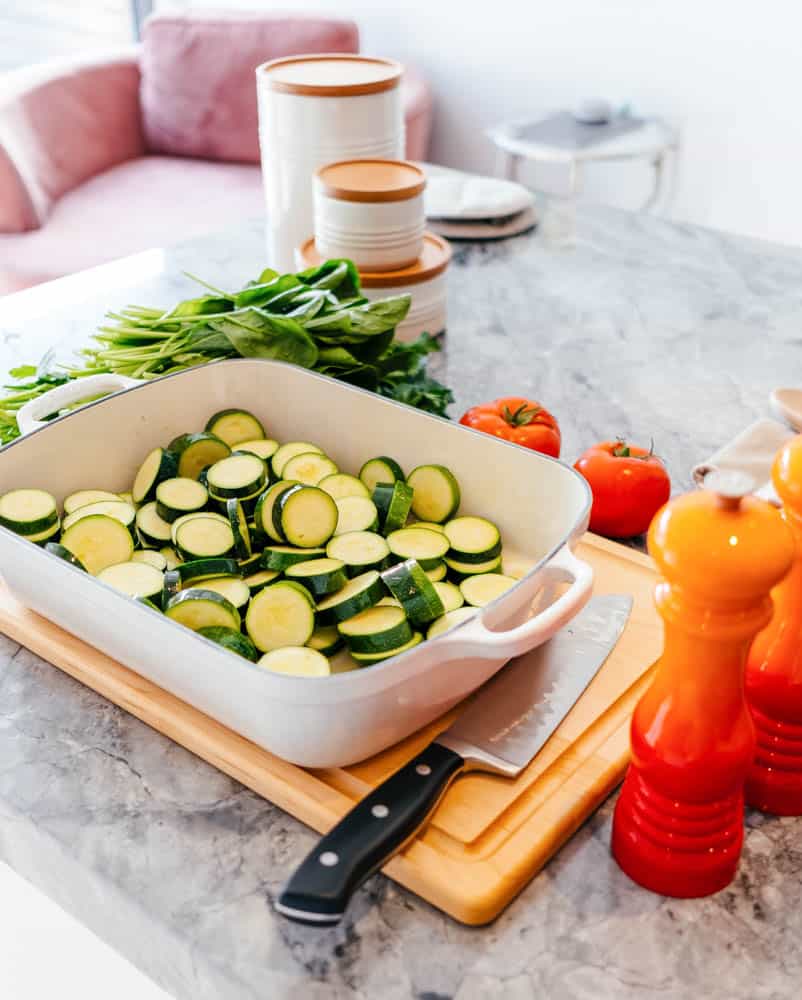 raising a kid who loves vegetables: sliced zucchini in a white porcelain baking dish, on a marble countertop