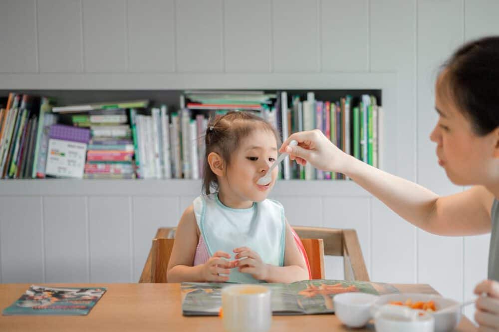 photo of mom feeding child with a spoon at the dinner table