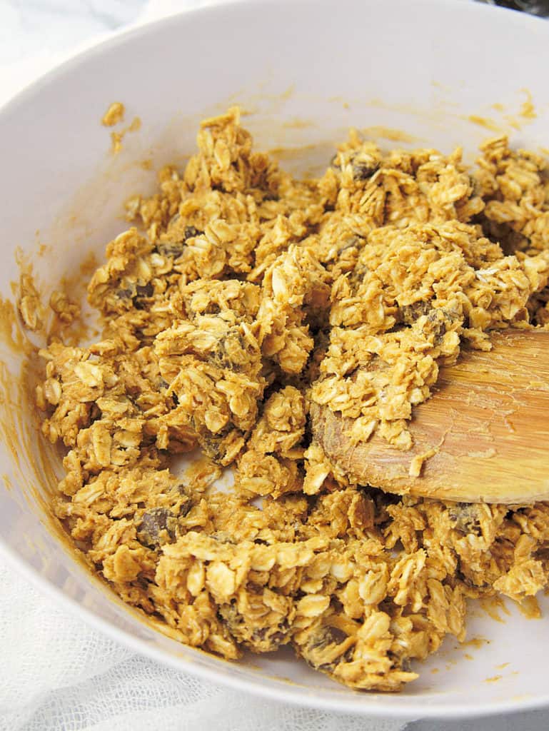 Wooden spoon stirring together the oats, peanut butter, chocolate chips, maple syrup, vanilla and salt until combined.