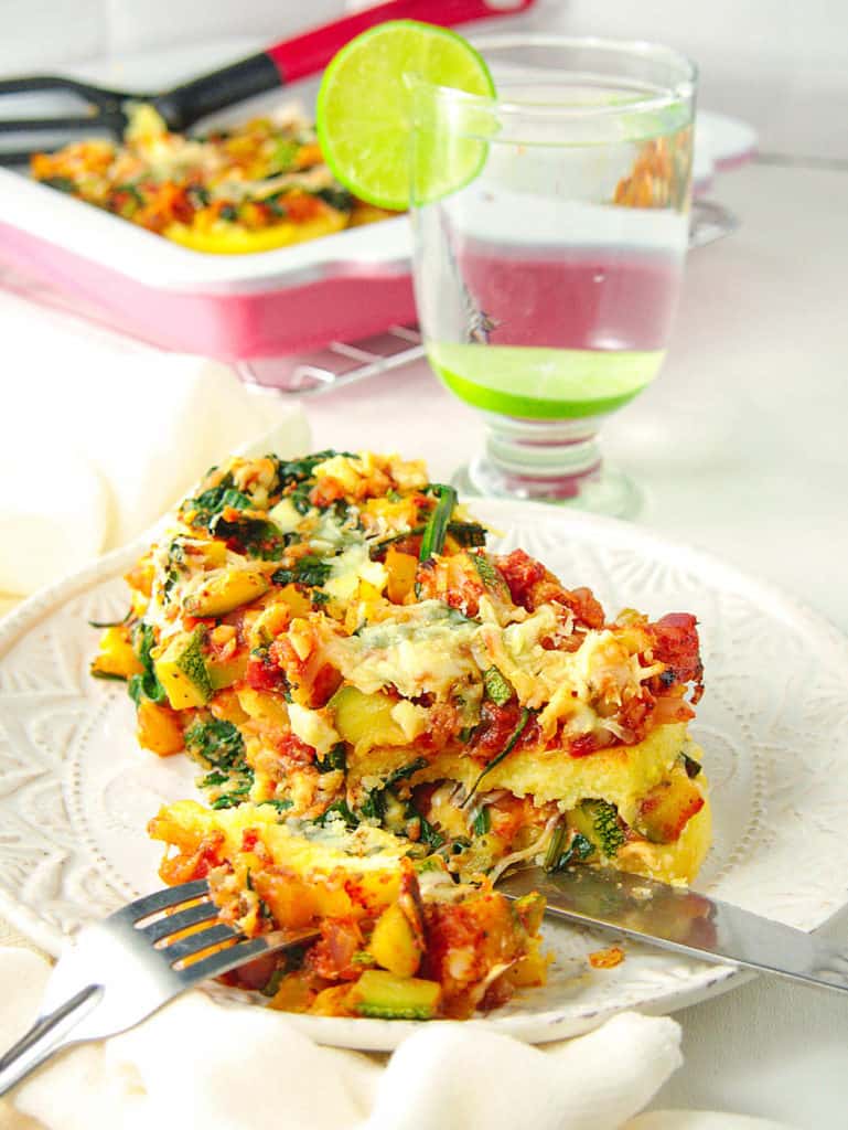 Gluten Free Lasagna with Polenta and Vegetables, cut and served on a white plate with the full casserole dish in the background