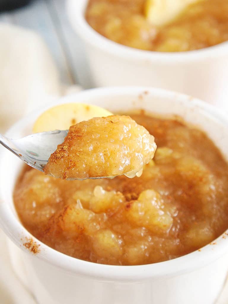 closeup of instant pot applesauce with cinnamon and honey, in a white ramekin with a sliced apple on top