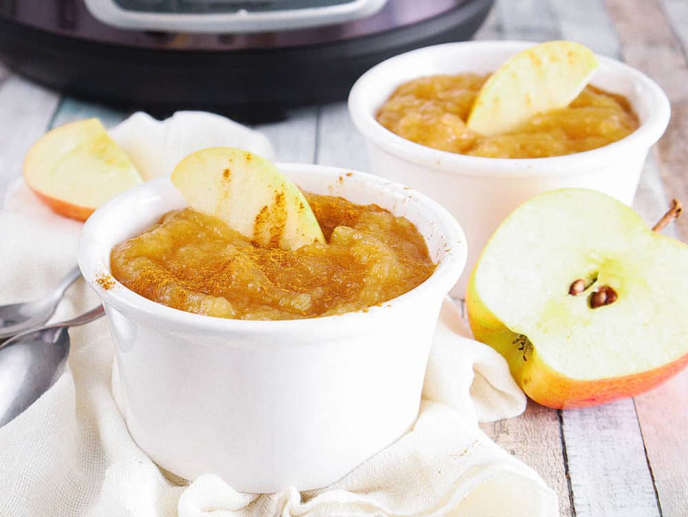 instant pot applesauce with cinnamon and honey, in a white ramekin with a sliced apple on top, pictured with an instant pot in the background