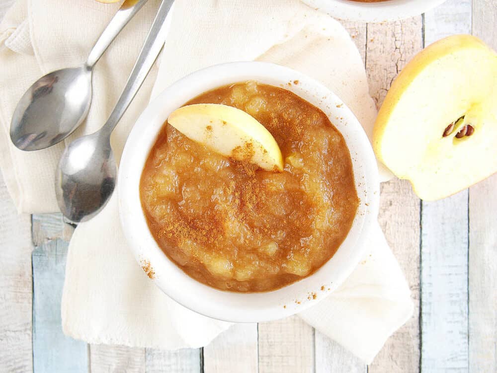instant pot applesauce with cinnamon and honey, in a white ramekin with a sliced apple on top, top view