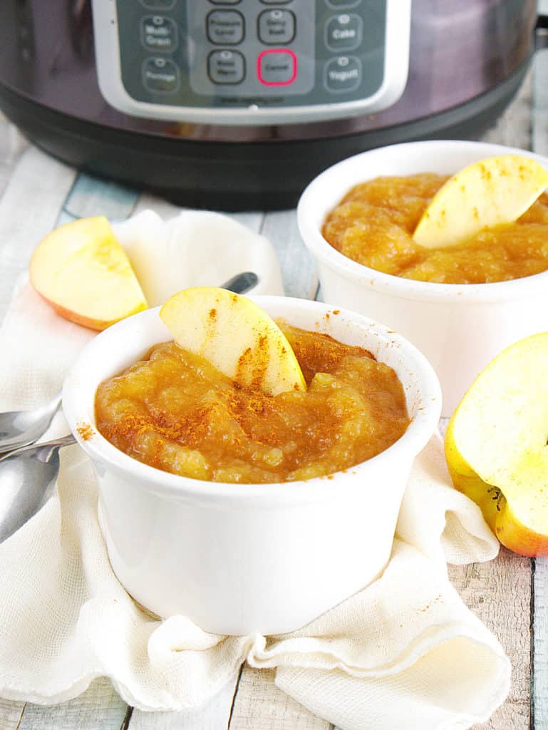 instant pot applesauce with cinnamon and honey, in a white ramekin with a sliced apple on top, pictured with an instant pot in the background