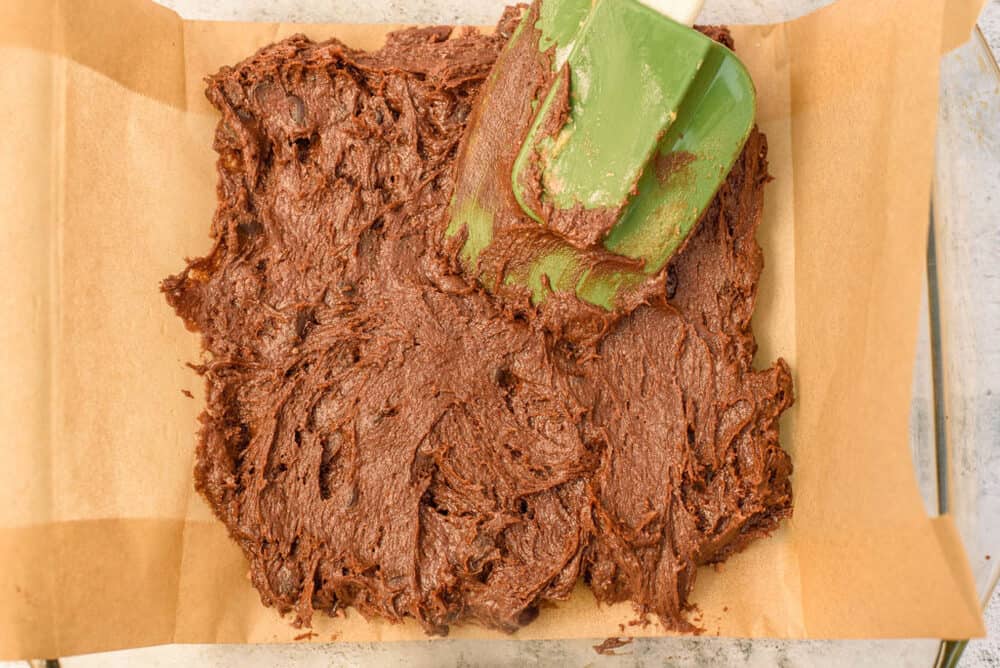 chocolate brownie layer spread into a baking pan lined with parchment paper