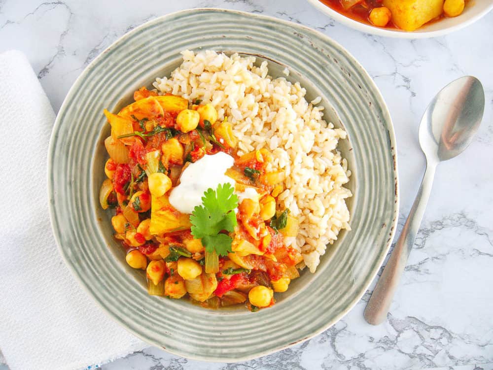 chickpea and potato curry served in a grey bowl, with brown rice on the side.