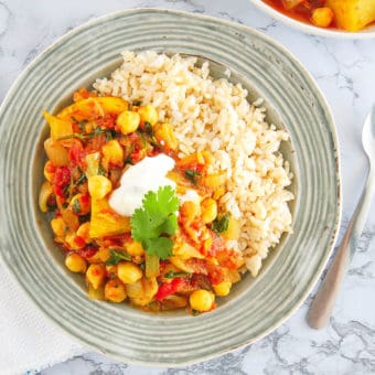 chickpea and potato curry served in a grey bowl, with brown rice on the side.