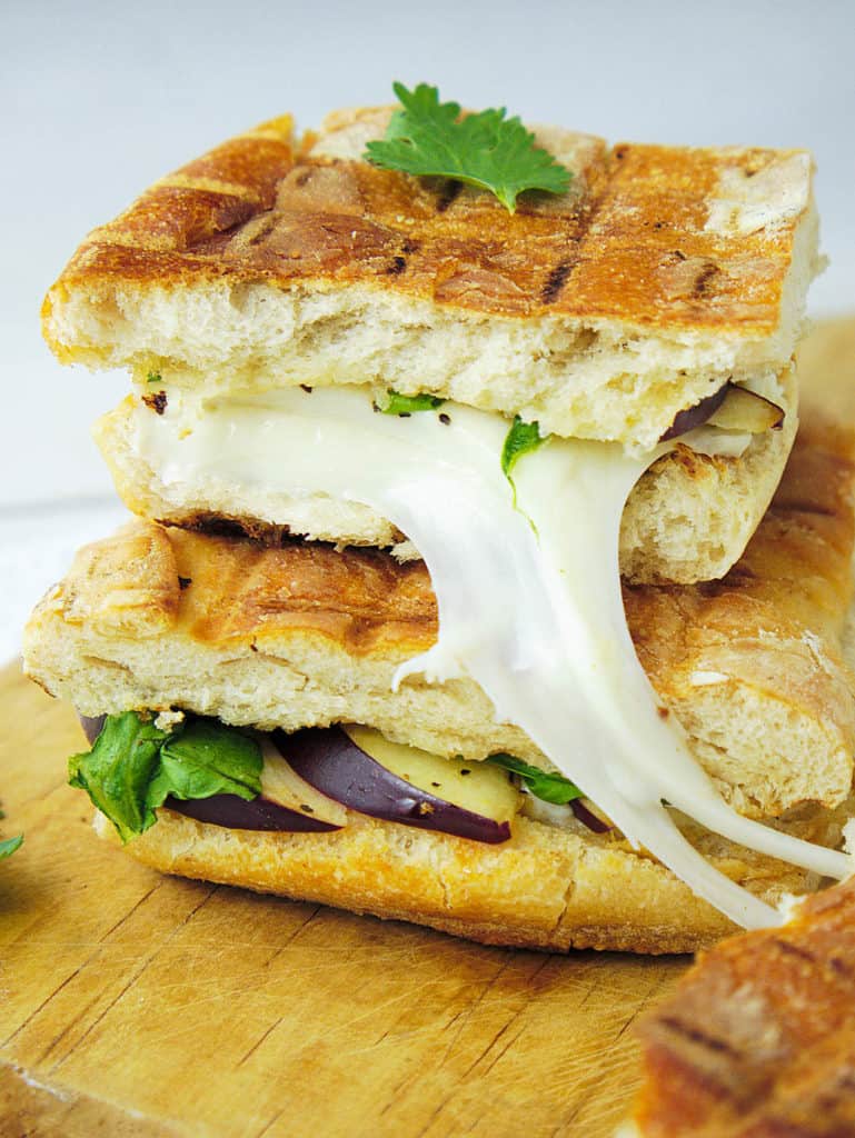 gourmet grilled cheese sandwich with brie and taleggio cheese, sliced pear, arugula, and honey - stacked on a wooden cutting board