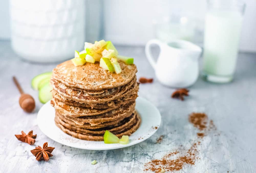 stacked apple cinnamon pancakes on white plate, with diced apple compote on top