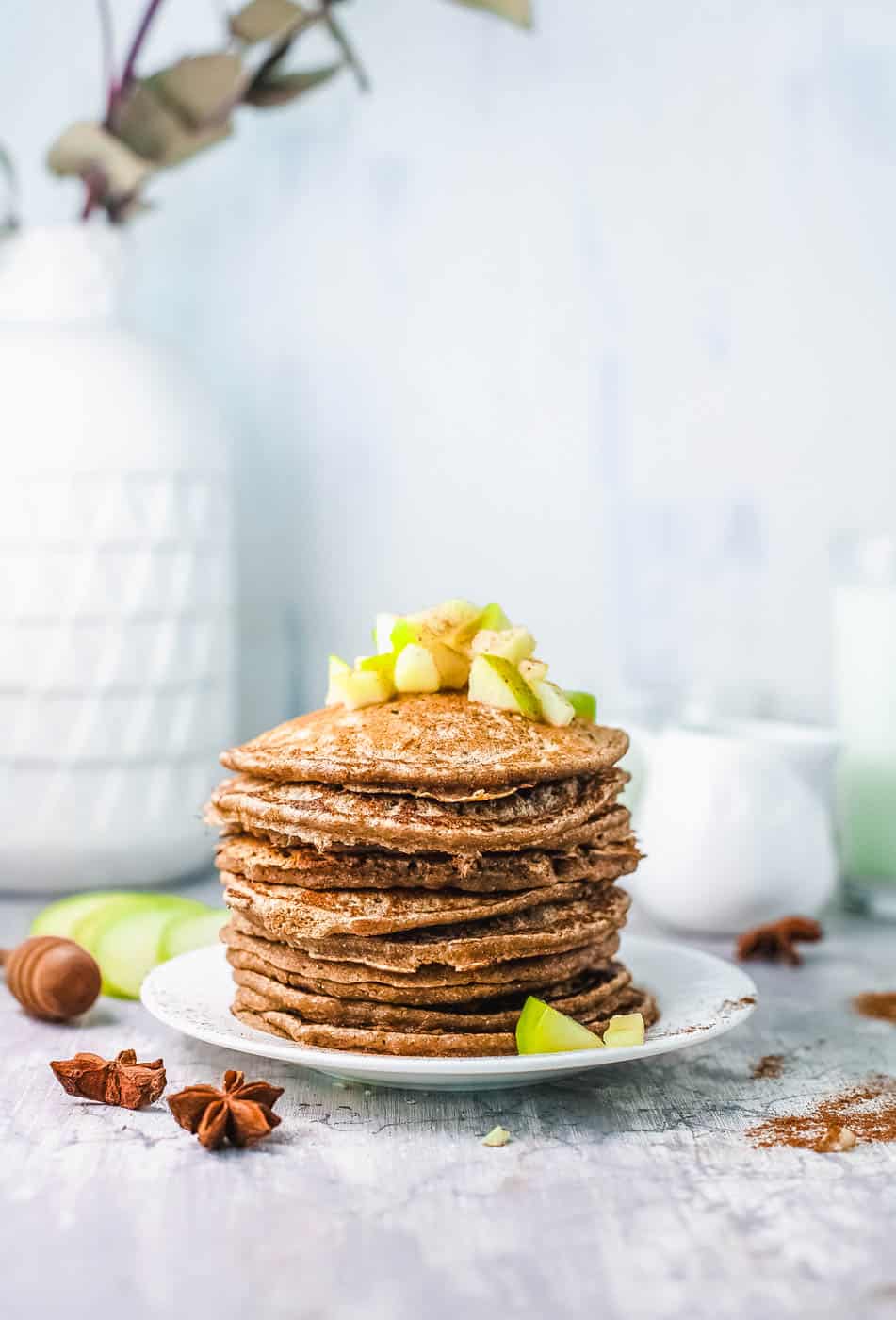 stacked apple cinnamon pancakes on white plate, with diced apple compote on top