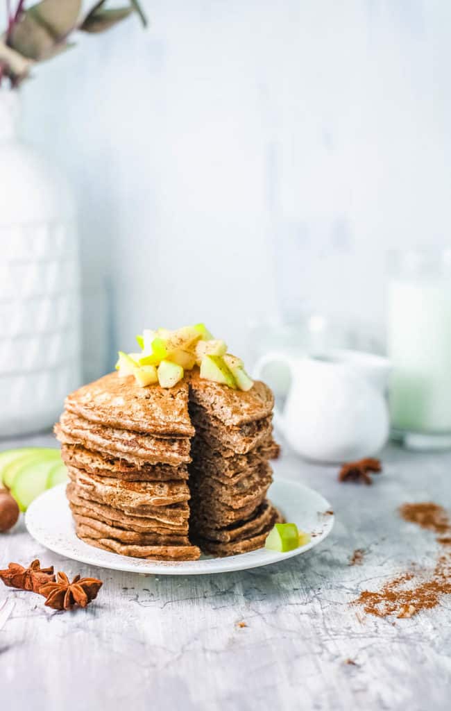 stacked apple cinnamon pancakes on white plate, with diced apple compote on top, cut into with a knife