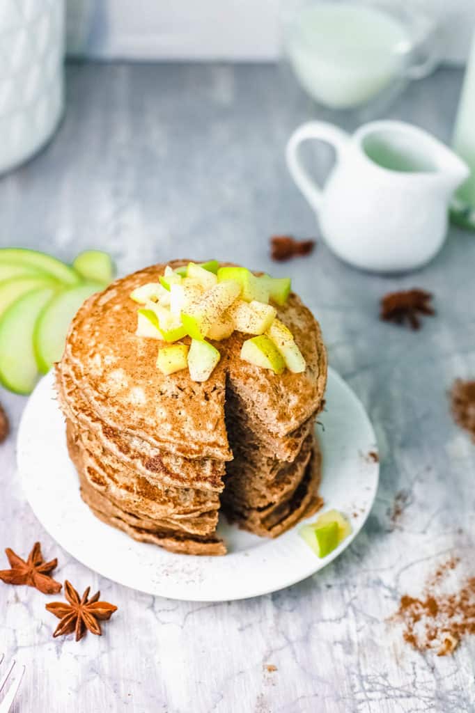 stacked apple cinnamon pancakes on white plate, with diced apple compote on top, cut into with a knife