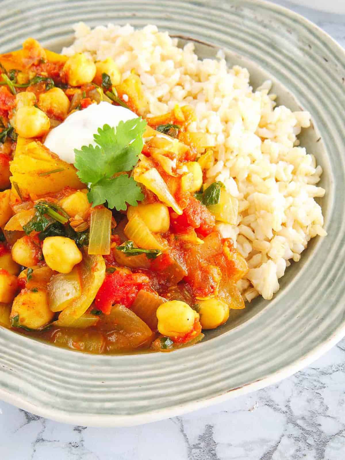 Chickpea and potato curry, served in a grey bowl with rice on the side. 