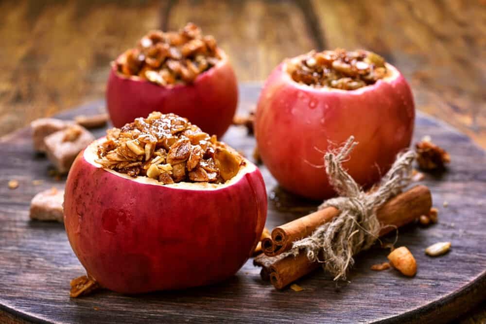 baked cinnamon apples stuffed with spiced sprouted quinoa, granola, nuts, fruit - on a grey plate