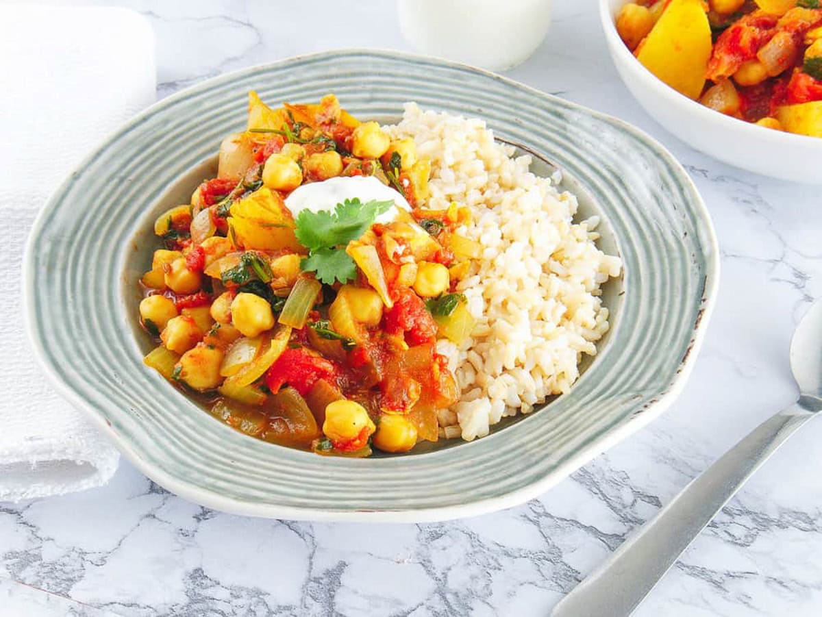 Chickpea and potato curry, served in a grey bowl with rice on the side.