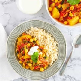 Chickpea and potato curry, served in a grey bowl with rice on the side, and an extra bowl of curry in the background.