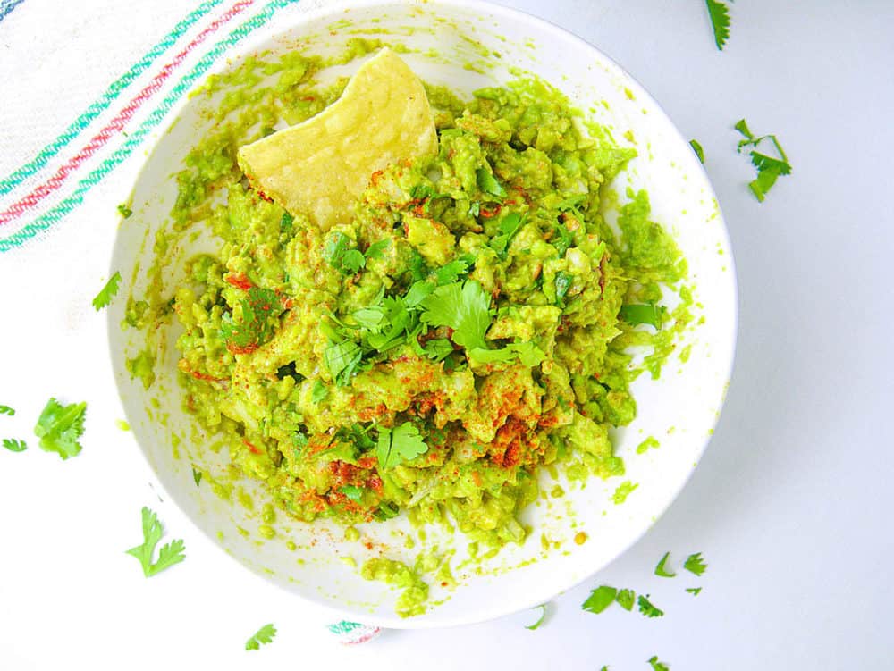healthy guacamole recipe in bowl with chip, top view