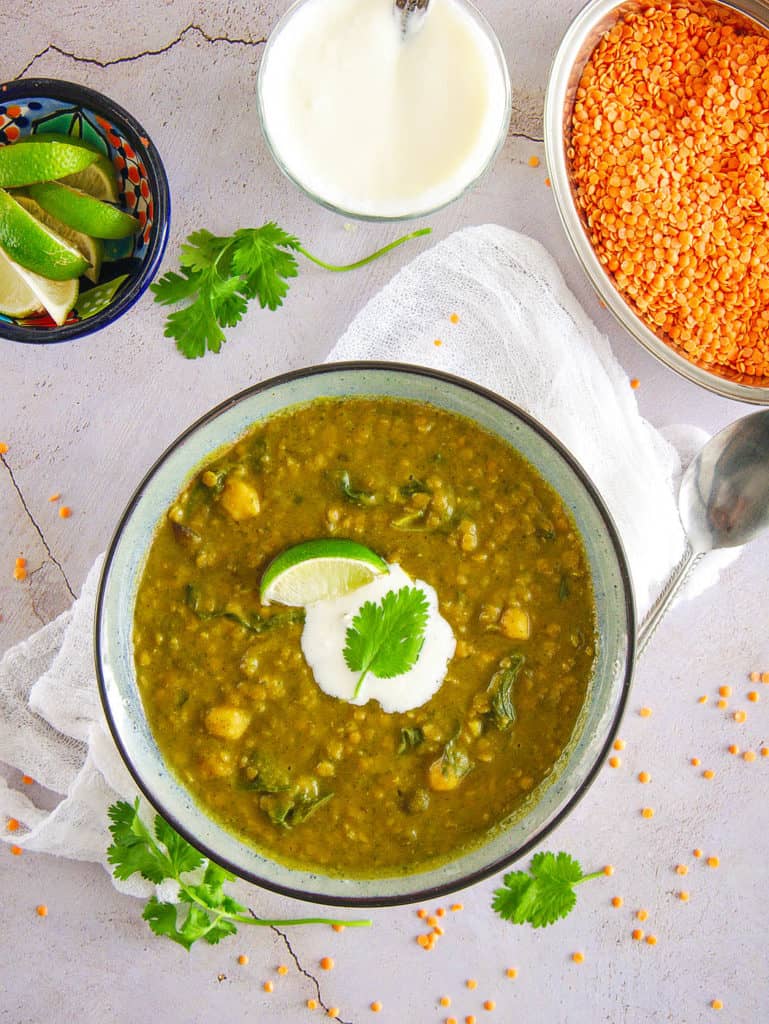 spicy indian lentil soup served in a blue bowl with lime, yogurt and lentils on the side - top view