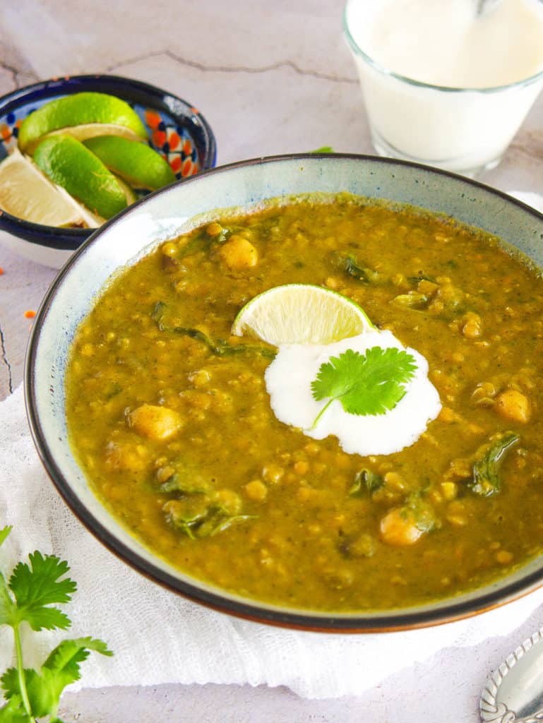 spicy indian lentil soup served in a blue bowl with lime, yogurt on the side - top view