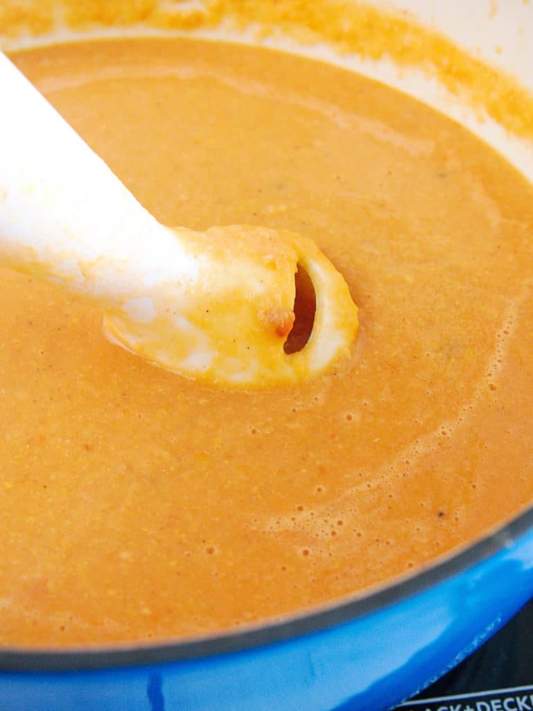 A closeup of an immersion blender in the pot of garbanzo bean soup.
