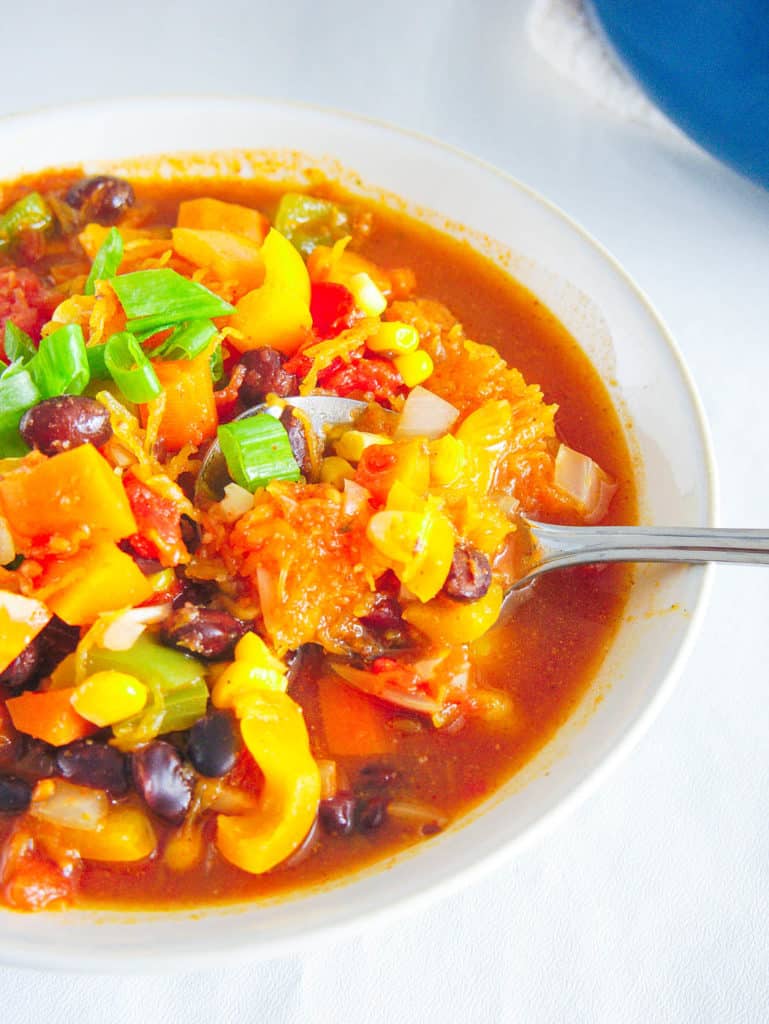 butternut squash chili served in a white bowl topped with green onions with a spoon