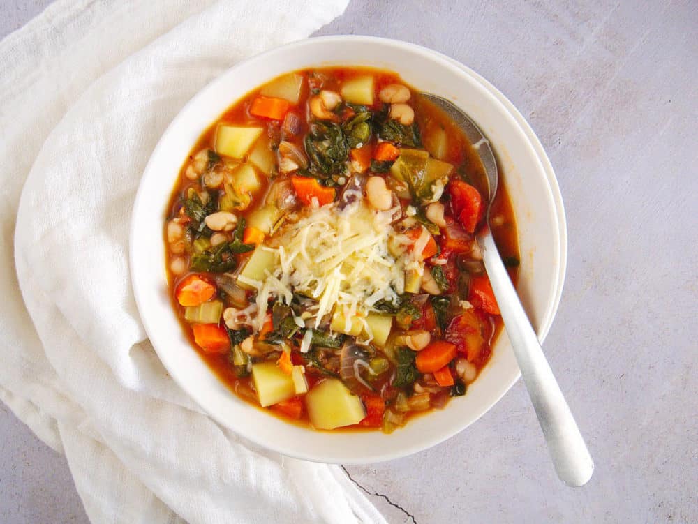 healthy minestrone soup in a white bowl with a spoon, top view
