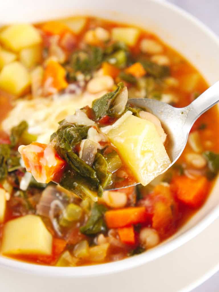 closeup of healthy minestrone soup in a white bowl with a spoon, topped with shredded parmesan cheese