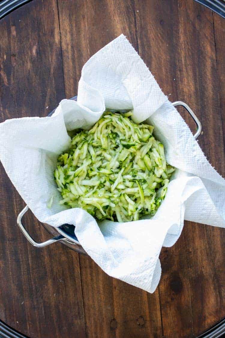Grated zucchini on a paper towel in a strainer