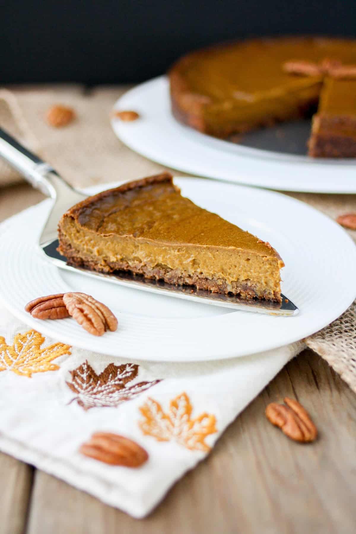 Front view of a slice of vegan pumpkin pie with pecan crust on a white plate