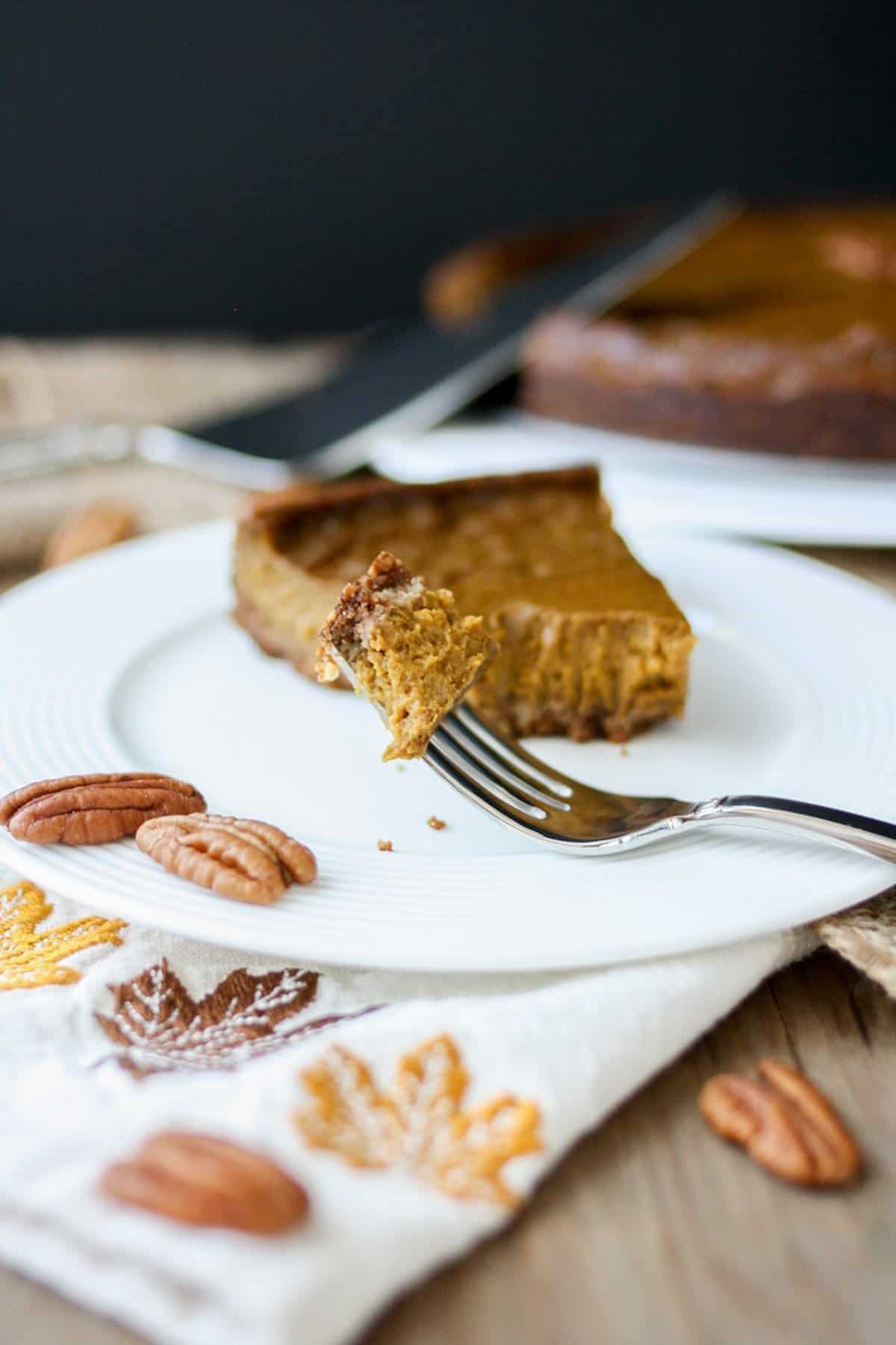 A slice of vegan pumpkin pie on a white plate with a bite of pie on a fork