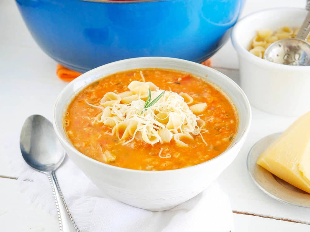 Chunky and Hearty Pinto Bean Soup in a white bowl, topped with parmesan cheese and pasta shells with spoon