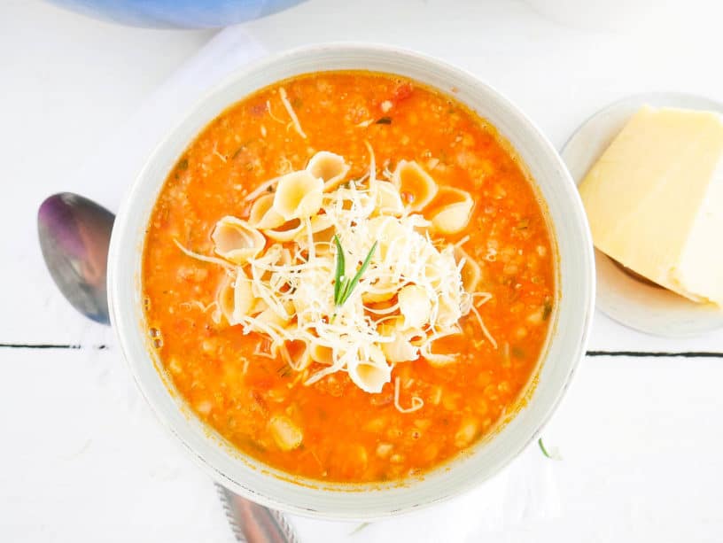 Chunky and Hearty Pinto Bean Soup in a white bowl, topped with parmesan cheese and pasta shells top view